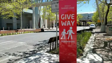 Red sign with "Give Way" and pedestrian icons on 'shared street' with 15kph speed limit in Canberra, Australia.